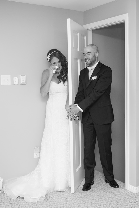 Bride and groom before the ceremony holding hands on separate sides of a door photograh in black and white
